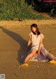 A woman sitting on a sandy beach in a dress.