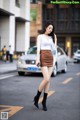 A woman in a white shirt and brown skirt is walking down the street.