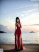 A woman in a red dress standing on a beach.