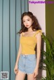 a woman in a yellow top and denim shorts posing for a picture
