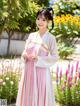 A woman in a pink and white hanbok standing in a garden.