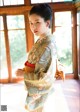 A woman in a kimono standing in front of a window.