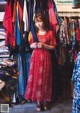 A woman in a red dress standing in front of a rack of clothes.