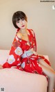 A woman in a red kimono sitting on a bed.