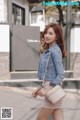 A woman in a denim jacket and pink shorts is walking down the street.