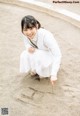 A little girl in a white dress crouching down on the ground.